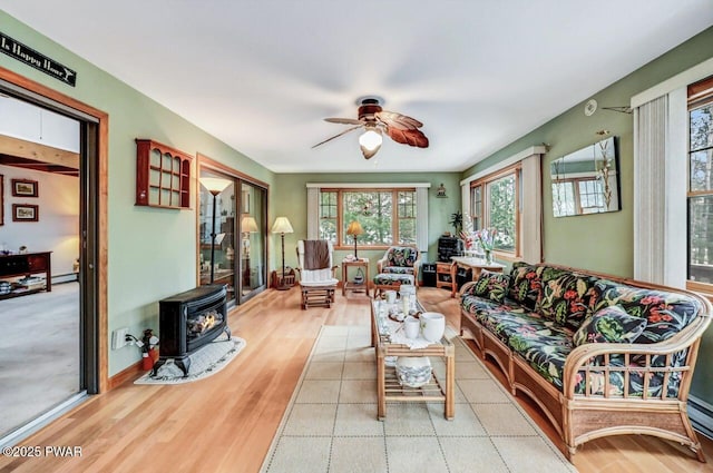 living room with ceiling fan, a wood stove, light wood-type flooring, and a baseboard radiator