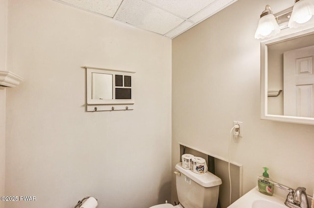 bathroom with toilet, sink, and a drop ceiling