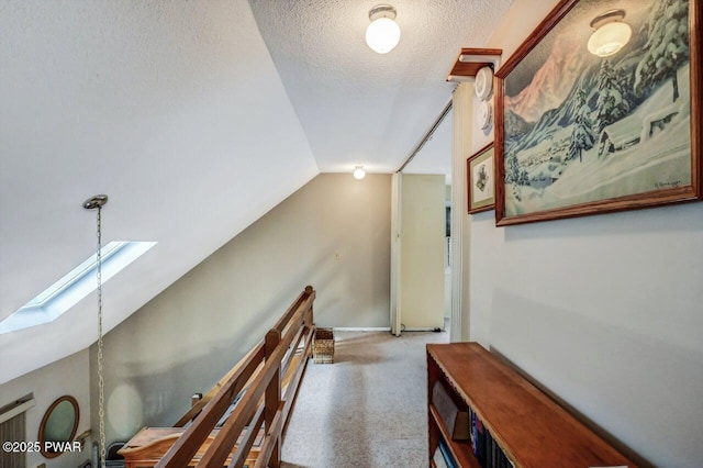 hall featuring carpet floors, vaulted ceiling with skylight, and a textured ceiling