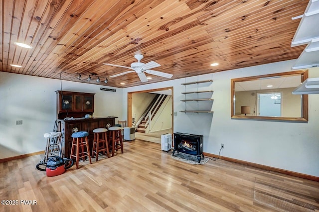 bar with rail lighting, a wood stove, wooden ceiling, and light hardwood / wood-style flooring