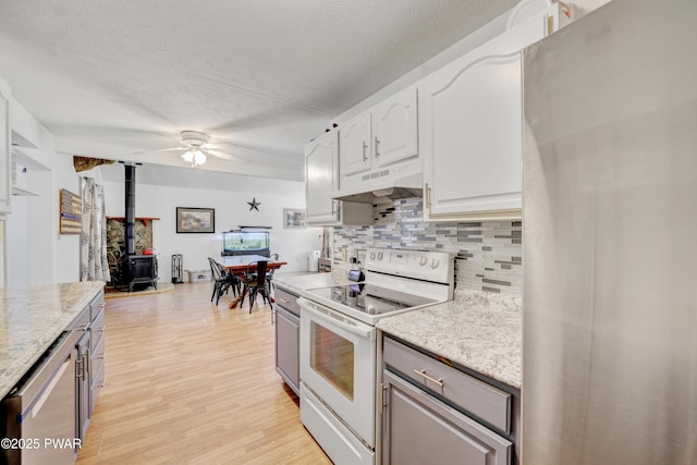 101 Bayberry Dr, Milford, PA 18337 - kitchen featuring stainless steel appliances, under cabinet range hood, decorative backsplash, a wood stove, and a ceiling fan