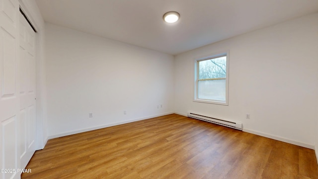 spare room with a baseboard heating unit, baseboards, and light wood finished floors