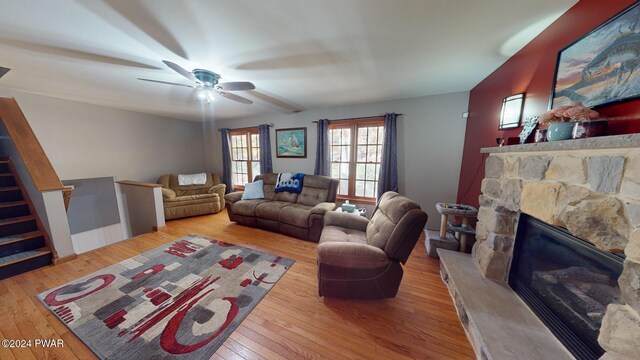 living room featuring light hardwood / wood-style flooring, a stone fireplace, and ceiling fan