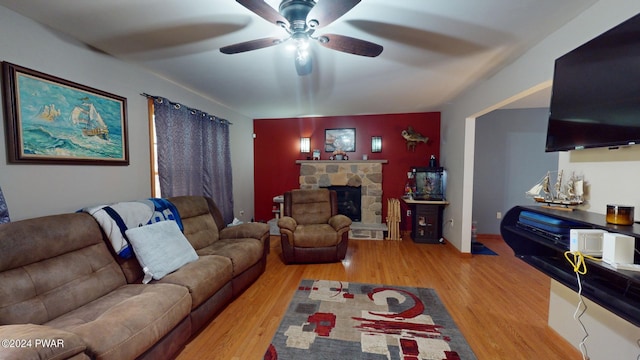 living room featuring a stone fireplace, ceiling fan, and light hardwood / wood-style floors