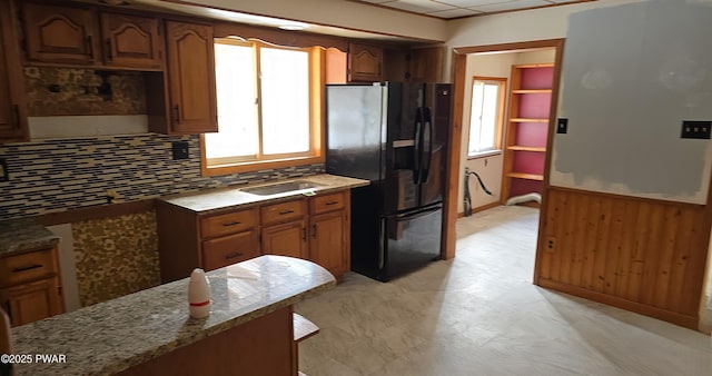 kitchen with freestanding refrigerator, decorative backsplash, dark stone counters, light floors, and brown cabinetry