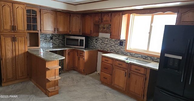 kitchen featuring light stone countertops, stainless steel microwave, brown cabinets, and black fridge with ice dispenser