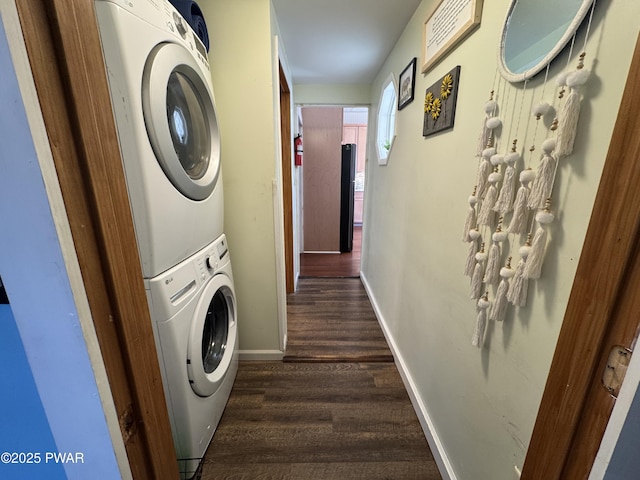 clothes washing area with stacked washer and dryer, baseboards, dark wood-style floors, and laundry area