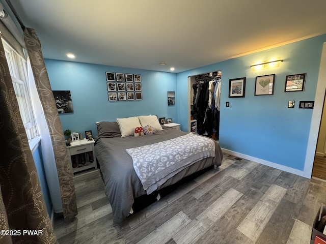 bedroom with wood finished floors, visible vents, baseboards, a spacious closet, and a closet