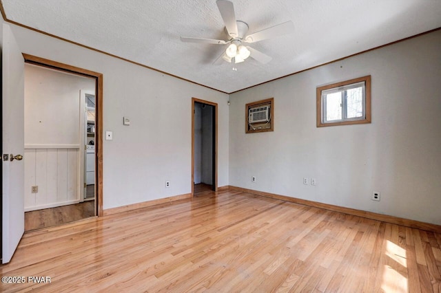 empty room featuring a textured ceiling, light wood-type flooring, an AC wall unit, ornamental molding, and a ceiling fan