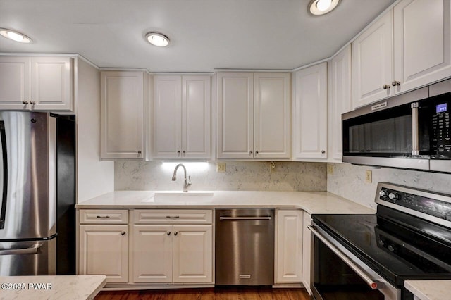 kitchen with white cabinetry, a sink, stainless steel appliances, light stone countertops, and wood finished floors