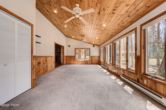 interior space with a wealth of natural light, a ceiling fan, wainscoting, wood walls, and baseboard heating