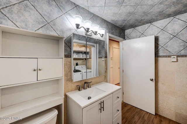 bathroom with toilet, washing machine and dryer, wood finished floors, and vanity