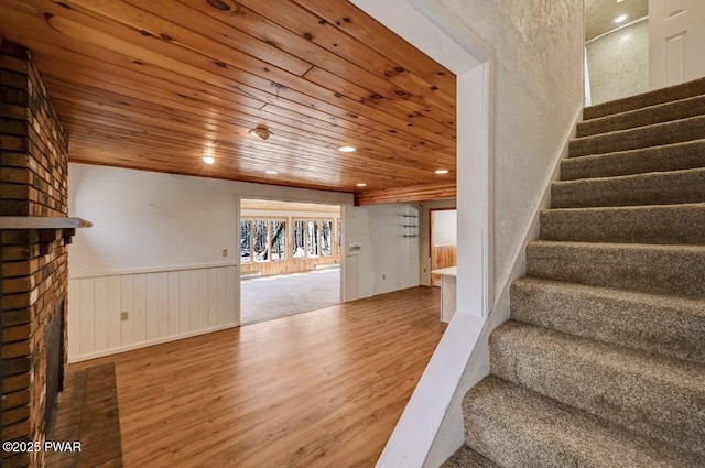 staircase featuring a wainscoted wall, wooden ceiling, recessed lighting, a fireplace, and wood finished floors