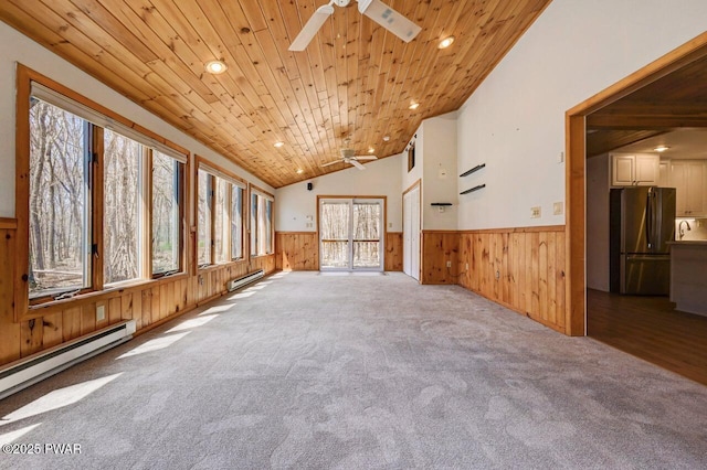 carpeted empty room with a wainscoted wall, a ceiling fan, baseboard heating, and wood walls