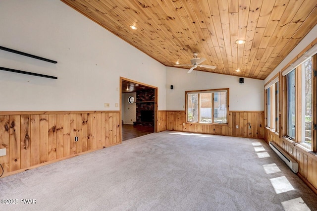 carpeted empty room featuring a ceiling fan, vaulted ceiling, wood walls, wainscoting, and a baseboard radiator