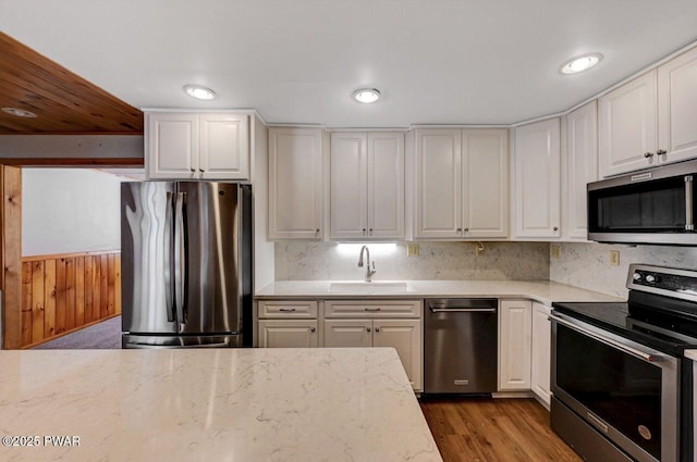 kitchen featuring light stone countertops, a sink, white cabinetry, appliances with stainless steel finishes, and wood finished floors