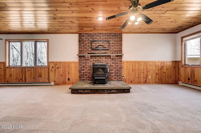 unfurnished living room featuring wood ceiling, a wood stove, baseboard heating, wooden walls, and wainscoting