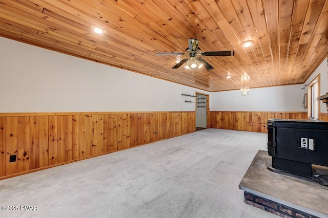 unfurnished living room featuring wooden ceiling, carpet, a wainscoted wall, a wood stove, and wooden walls