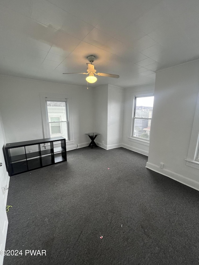 empty room featuring ceiling fan, dark carpet, and a healthy amount of sunlight