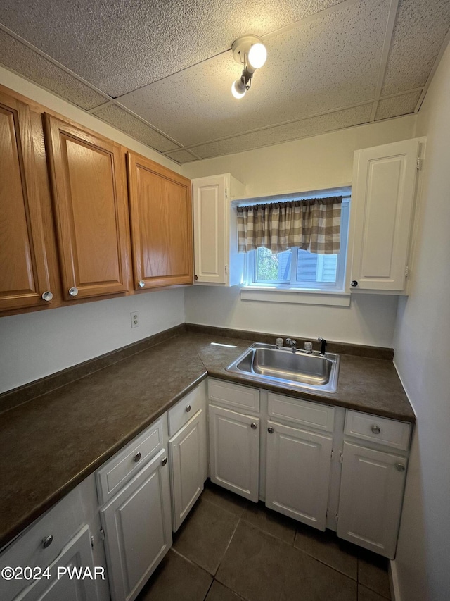 kitchen featuring sink, white cabinets, a drop ceiling, and dark tile patterned flooring