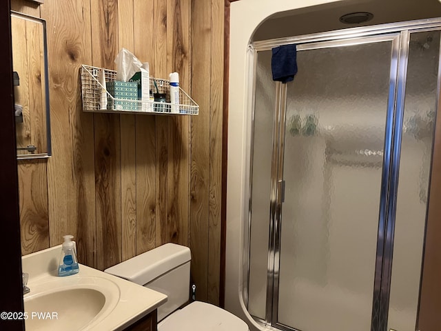 bathroom with toilet, wood walls, a shower stall, and vanity