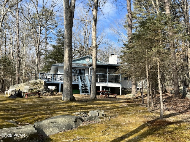 back of property featuring stairway, a sunroom, a chimney, and a wooden deck