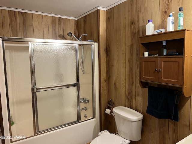 bathroom featuring combined bath / shower with glass door, toilet, and wooden walls