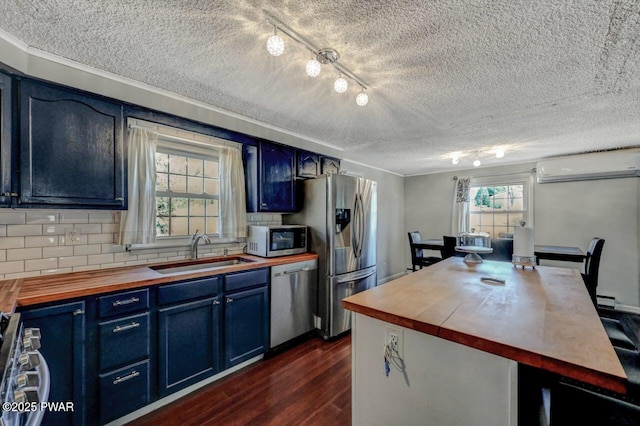 kitchen featuring blue cabinets, appliances with stainless steel finishes, a wall mounted air conditioner, and butcher block counters