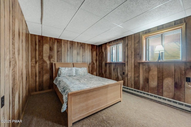 bedroom featuring a baseboard heating unit, wooden walls, and carpet