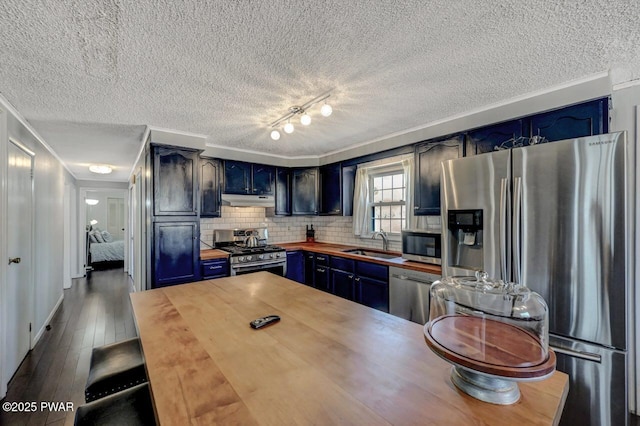 kitchen featuring under cabinet range hood, blue cabinets, appliances with stainless steel finishes, and butcher block countertops