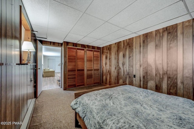 unfurnished bedroom with baseboard heating, a drop ceiling, carpet, and wood walls