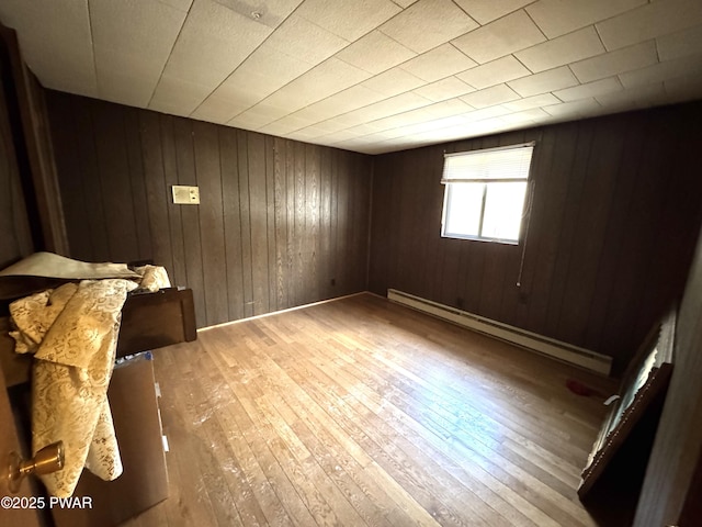 spare room with a baseboard heating unit, light wood-type flooring, and wood walls