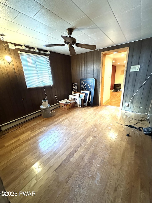 interior space featuring ceiling fan, hardwood / wood-style floors, wooden walls, and a baseboard radiator