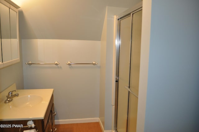 bathroom with wood finished floors, vanity, baseboards, vaulted ceiling, and a shower stall