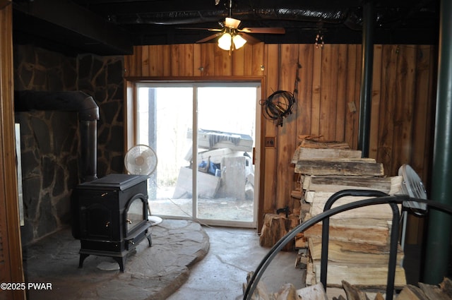 interior space featuring a wood stove, wood walls, and ceiling fan