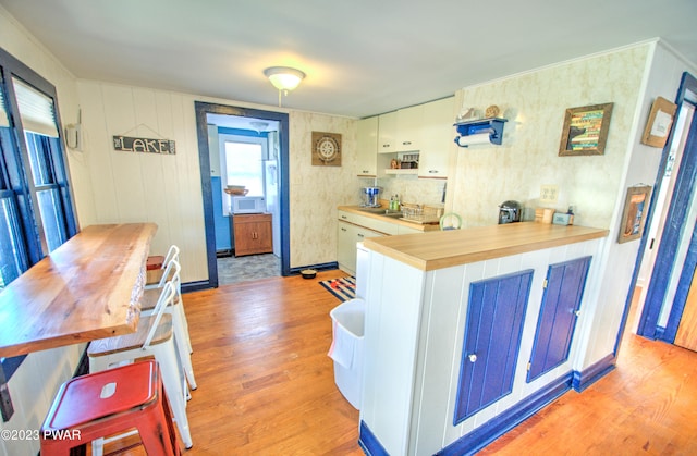 kitchen with wooden counters, sink, wooden walls, light hardwood / wood-style floors, and white cabinetry