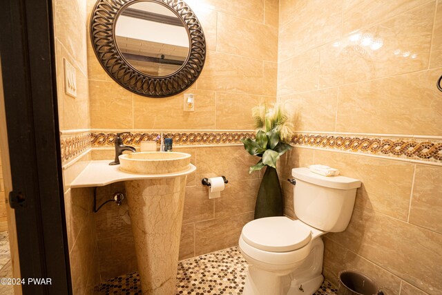 bathroom with toilet, sink, and tile walls