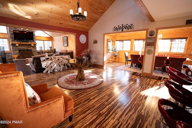 living room featuring wood-type flooring, beam ceiling, high vaulted ceiling, a chandelier, and a stone fireplace