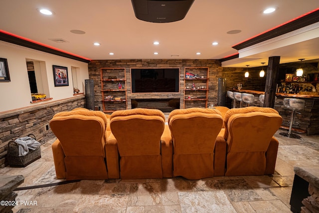 cinema room with a stone fireplace, built in shelves, indoor bar, and ornamental molding