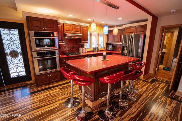 kitchen featuring appliances with stainless steel finishes, tasteful backsplash, a center island, dark hardwood / wood-style floors, and a breakfast bar area