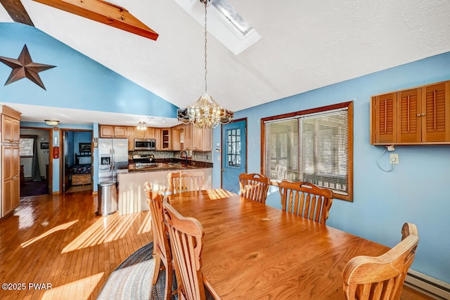 dining room featuring dark wood-type flooring, a skylight, a chandelier, high vaulted ceiling, and a baseboard heating unit