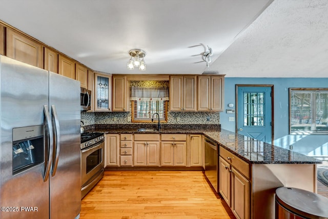 kitchen with appliances with stainless steel finishes, plenty of natural light, dark stone counters, and kitchen peninsula