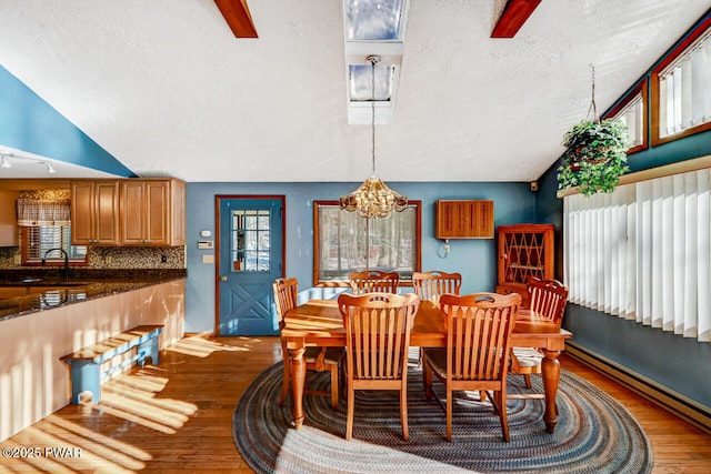 dining room with wood-type flooring, a baseboard heating unit, a textured ceiling, and a notable chandelier