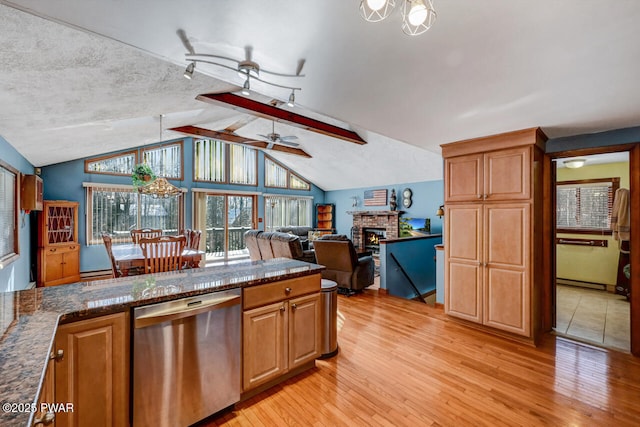 kitchen with light hardwood / wood-style flooring, dark stone countertops, vaulted ceiling with beams, a stone fireplace, and stainless steel dishwasher