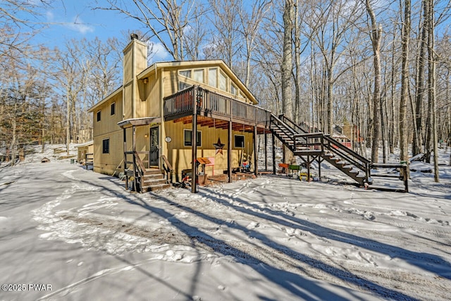 view of snow covered exterior with a chimney, a deck, and stairs