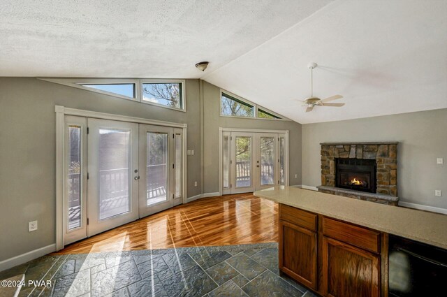 interior space featuring ceiling fan, french doors, vaulted ceiling, a textured ceiling, and a fireplace