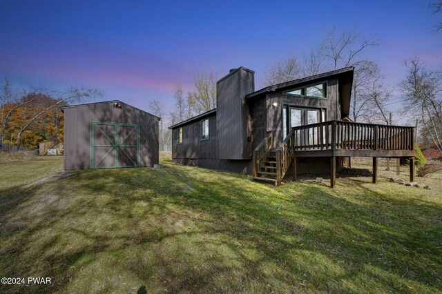 back house at dusk featuring a yard, an outdoor structure, and a wooden deck