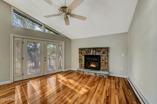 unfurnished living room with vaulted ceiling, baseboard heating, ceiling fan, hardwood / wood-style flooring, and a stone fireplace