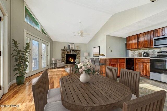 dining room with lofted ceiling, french doors, a stone fireplace, light hardwood / wood-style flooring, and ceiling fan