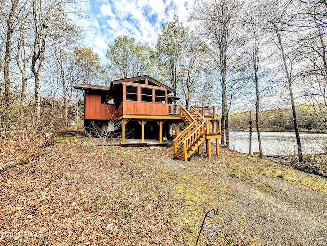 back of house featuring stairs, a deck with water view, and a sunroom